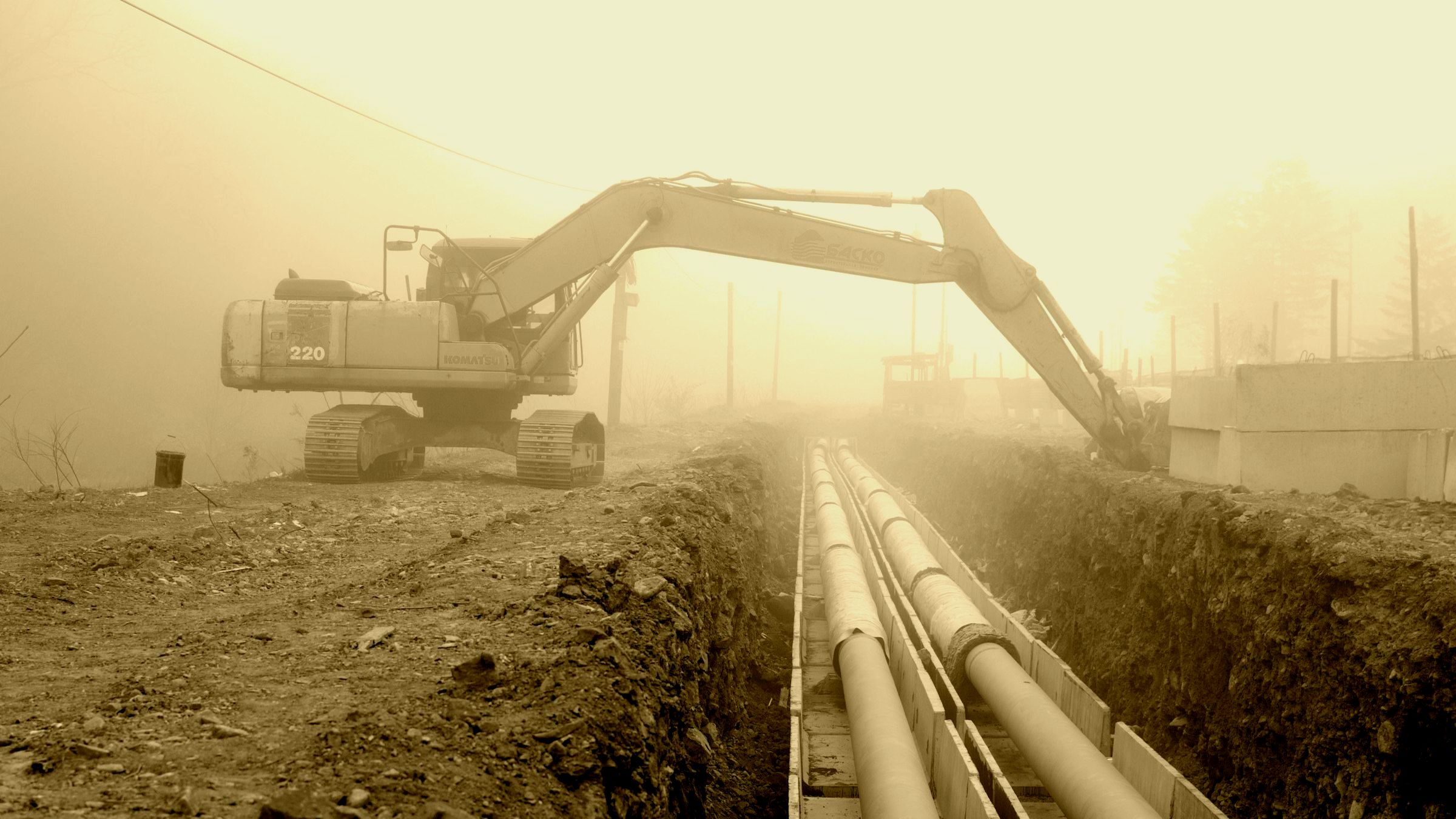 Excavator laying a steel pipeline along an open trench